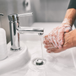 Person washing hands with soap under a modern faucet, emphasizing hygiene practices in a clean bathroom setting.